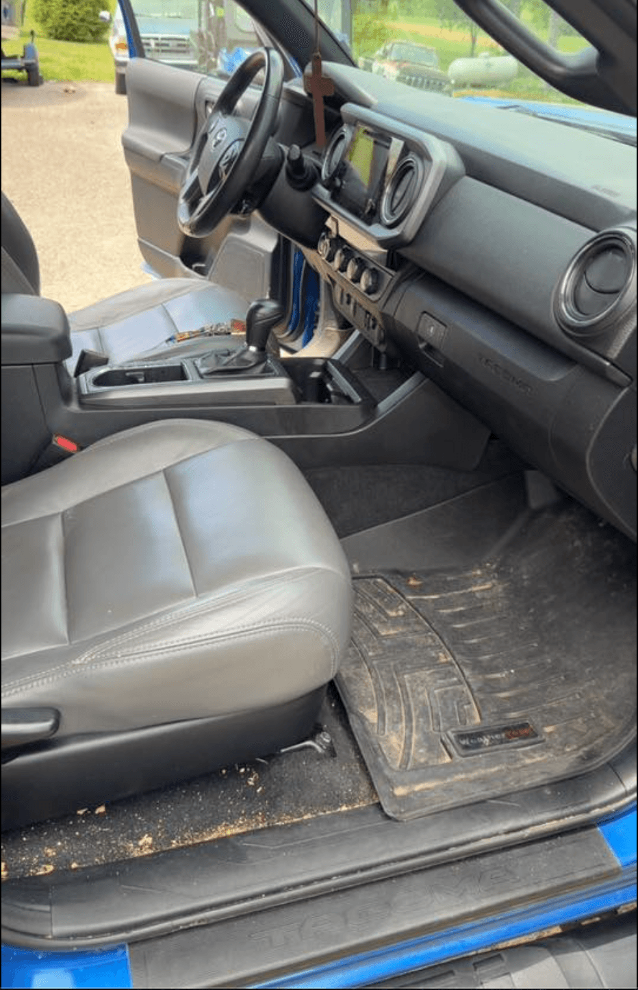 Toyota Tacoma driver-side floor with grass clippings and dirt on the rubber mat before interior detail